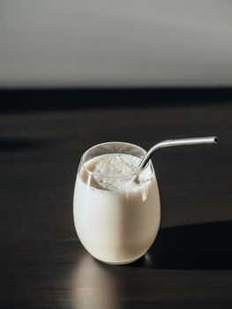 Protein milkshake in tumbler glass with metal straw over black background. Vertical. Copy space for text or design.