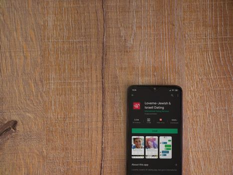Lod, Israel - July 8, 2020: Loveme app play store page on the display of a black mobile smartphone on wooden background. Top view flat lay with copy space.