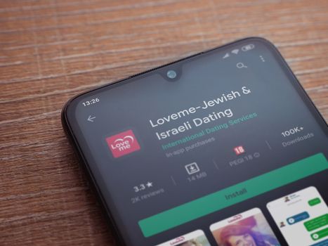 Lod, Israel - July 8, 2020: Loveme app play store page on the display of a black mobile smartphone on wooden background. Top view flat lay with copy space.