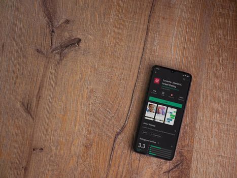 Lod, Israel - July 8, 2020: Loveme app play store page on the display of a black mobile smartphone on wooden background. Top view flat lay with copy space.