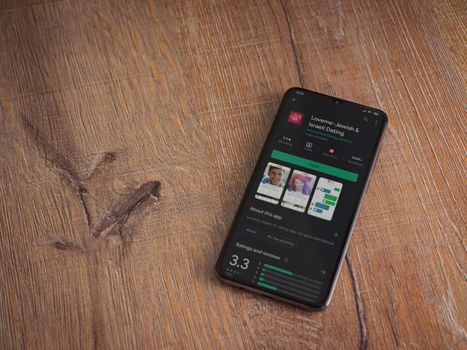 Lod, Israel - July 8, 2020: Loveme app play store page on the display of a black mobile smartphone on wooden background. Top view flat lay with copy space.