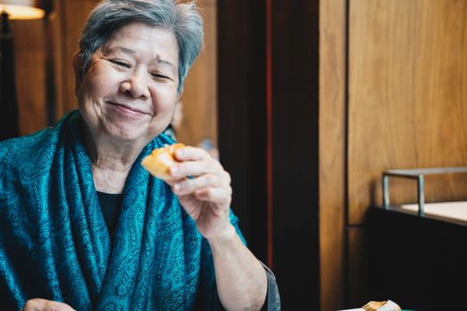 old asian elderly senior elder woman eating bread at restaurant. mature retirement lifestyle