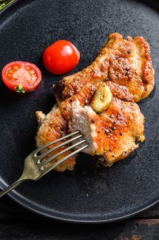 Dish of grilled pork chop with tomatoes top view with knife and slice on fork over old rustic dark wood table table close up top view.