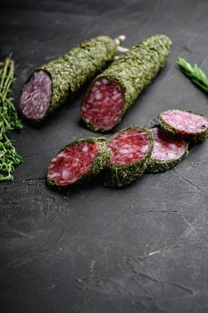 Fuet salami sausage in herbs on black textured surface.