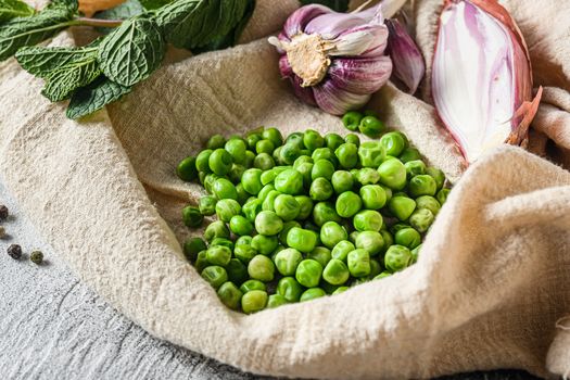 organic green peas for mushypeas and ingredients peas mint shallot pepper and salt keto food photo over grey stone background and cloth side view close up.