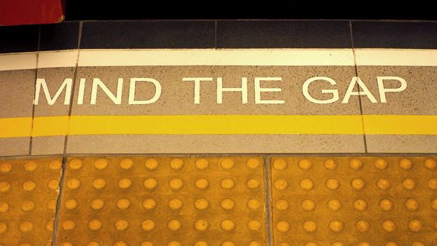 Mind the gap sign on the subway train platform floor and yellow color and dirty and no people.