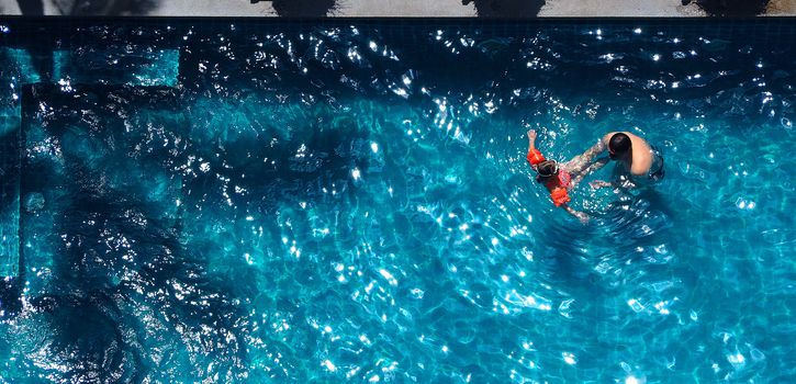 Happy dad and young daughter playing together in swimming pool with life ring for safety on sunny summer day.