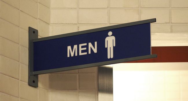 Toilet sign plastic tab with white and blue color and hanging by grey steel metal on the old dirty wall tile.