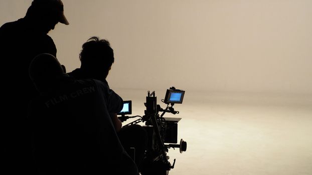 Silhouette of working people or production film crew are making movie or shooting tv online content live show in studio with camera equipment set.