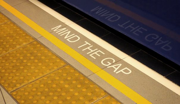 Mind the gap sign on the subway train platform floor and yellow color and dirty and no people.