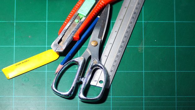 Scissor and cutter and ruler and pencil and blades on the green cutting mat and top view angle camera.