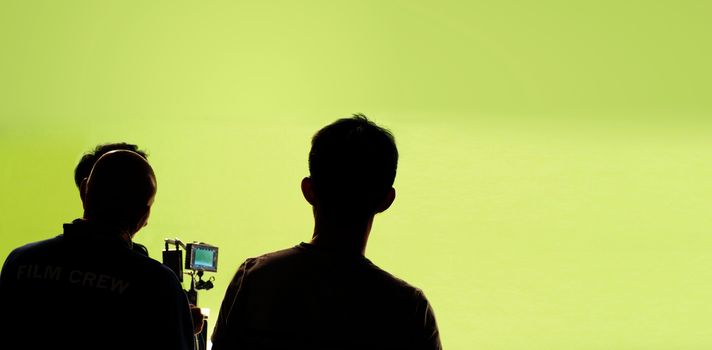 Behind the video production camera set and crew team shooting in a big green screen studio.