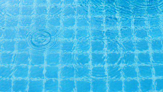 Rain drops on the swimming pool blue water surface that have ripple wave effect on liquid texture and top view angle.