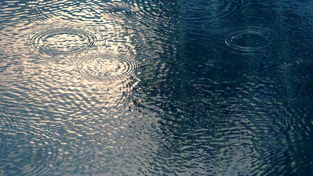 Rain drops on blue water swimming pool top view and sun light reflect on the texture.