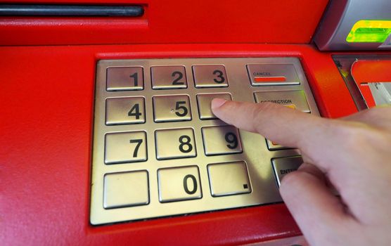 ATM machine red color and finger hand touch on number button for withdrawal and close-up shot.