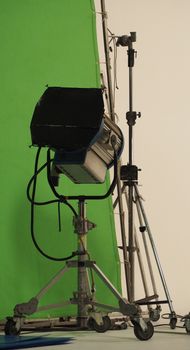 Studio spotlight big size equipment on the tripod in a huge studio with green screen background .