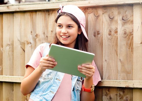 girl in a pink baseball cap with a tablet smiling outdoors