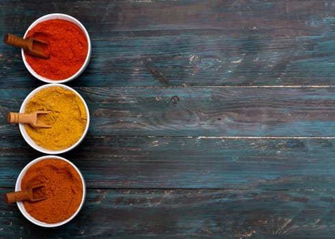 Colorful spices in white bowls and wooden spoons on wooden background