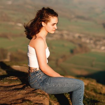 A girl sitting on top of the hill against amazing landscape in the summer