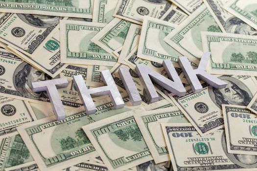 The word think laid with aluminium letters on the US dollar banknotes background - with selective focus.