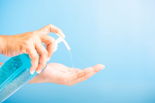 Close up Asian young woman applying press dispenser sanitizer alcohol gel pump to hand wash cleaning, hygiene prevention COVID-19 or coronavirus protection concept, isolated on blue background