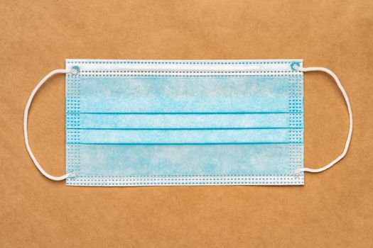 Blue medical surgical face mask with rubber ear straps on yellow craft paper background. Flat lay, close-up view.