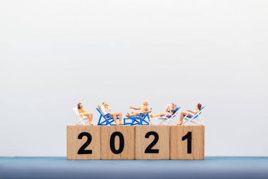 Miniature people wearing swimsuit sitting on the lounge chair at wooden block 2021