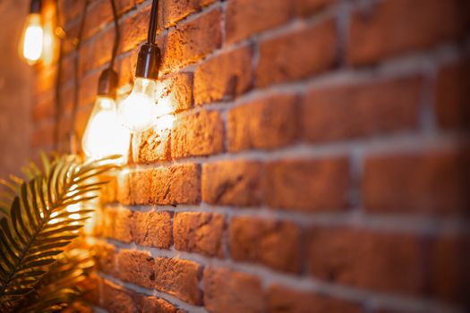 A brick wall with a burning light bulb that creates coziness and New Year's mood. Garland and Christmas tree