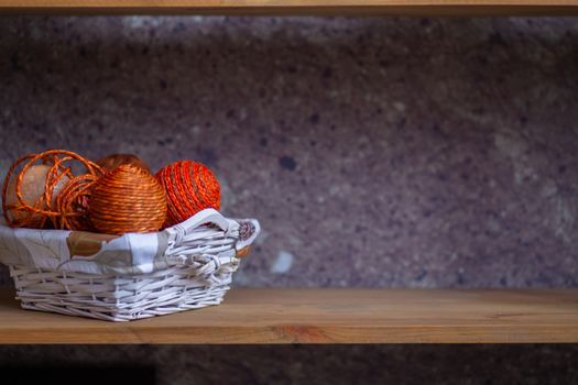 A wicker basket with orange balls of thread or rope folded into it. The handmade basket is on the shelf