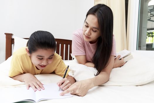 Asian family mother and her daughters doing homework  together on bed in bedroom. family and learn at home concept.