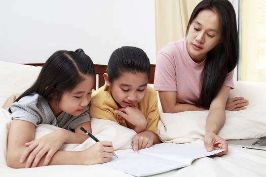 Asian family mother her daughters do homework  together on bed in bedroom. family and learn at home concept.