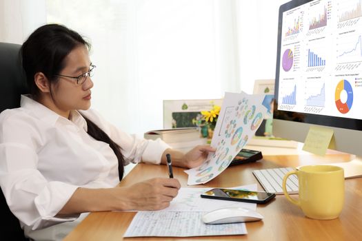 Business woman working in office with computer holding chart report paper and looking. business people working at home with paper and PC screen. Business and finance ,work at home concept