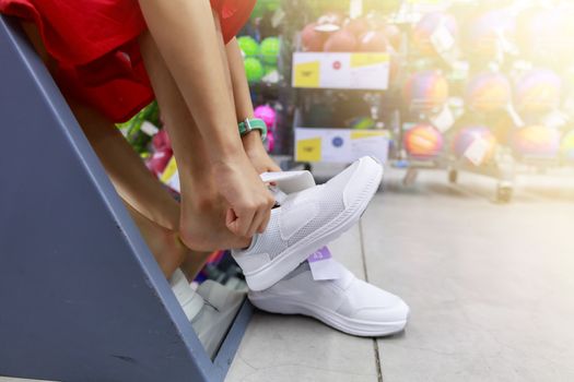 Little girl tried shoe in front of mirror in shopping mall. Asian girl smileing happy to choice and tried sneaker in front of mirror in shop with copy space. Girl holding  sneaker for tried.