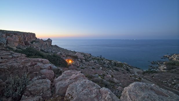 A campfire burns just after sunset at the rocky coastline of Selmun in Malta