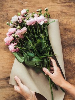 Top view on wooden table with roses, craft paper and pink ribbon on it. Florist work place. Accessories for making bouquets and floral compositions.