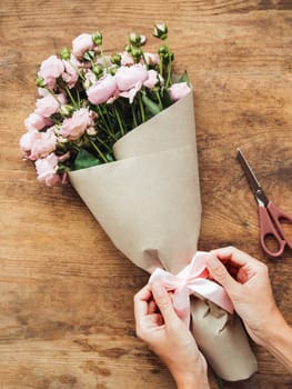 Top view on wooden table with roses, scissors, craft paper and pink ribbon on it. Florist work place. Accessories for making bouquets and floral compositions.