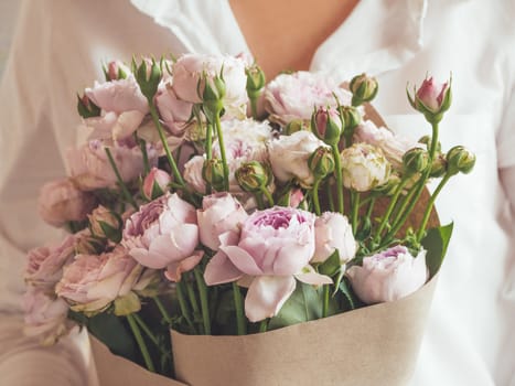 Woman in white shirt holds bouquet of lilac colored roses.