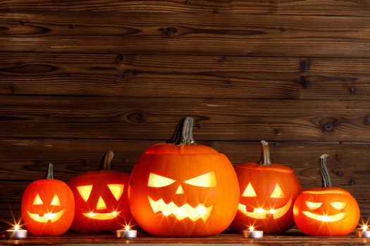 Halloween pumpkin head lanterns and burning candles on wooden background