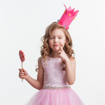 Beautiful excited candy princess girl in crown holding big lollipop and making a wish