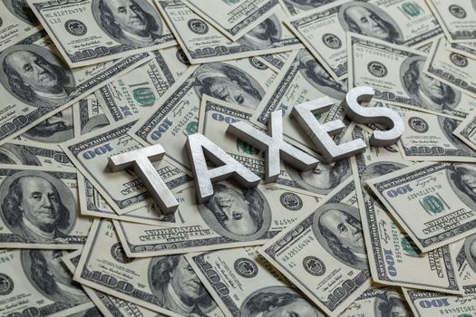 The word taxes with aluminium thick letters on the US dollar bills background - with selective focus.
