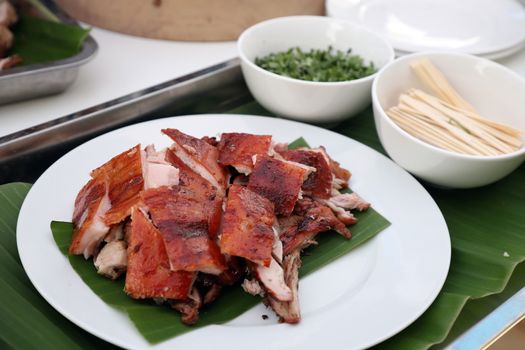 Roasted suckling pig, crispy skin, cut into pieces Looks delicious on a white plate, beneath the pork with banana leaves. Selective focus.