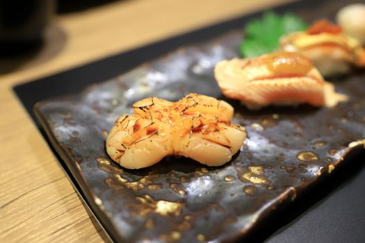 Sushi topped with hotate scallop, burns a little. Then smeared with special sauce On a traditional Japanese plate in a Japanese restaurant. Selective focus.