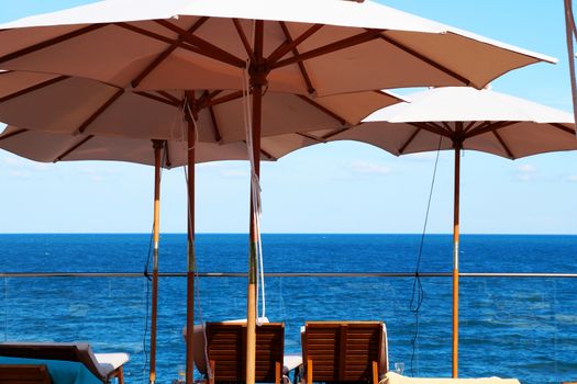 two sun loungers under an umbrella on the outdoor patio against the background of the sea horizon