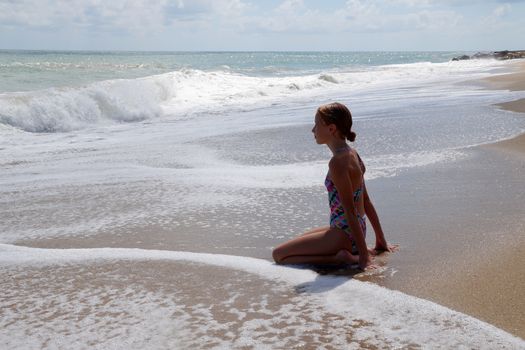 teenage girl sitting alone on the wet sand and looking at the sea.