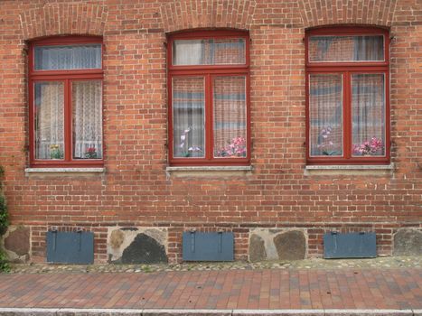 Three windows with red painted frames in a brick wall, Mecklenburg-Western Pomerania, Germany.