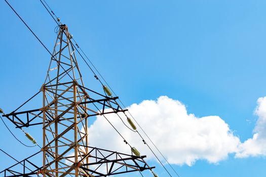 A metal power line support with insulators and wires used to support an overhead power line against white cloud and blue sky background, copy space.