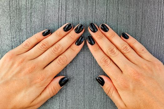Beautiful female hands with beautiful black manicure nails, beautiful black with shine on a gray striped background textile.