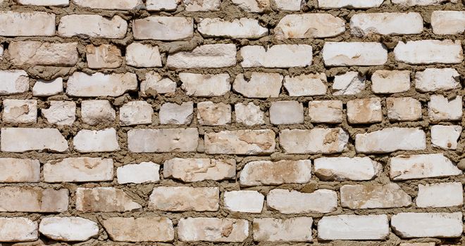 Hard sunlight on the dirty texture of a wall of old white brick and mortar, close-up.