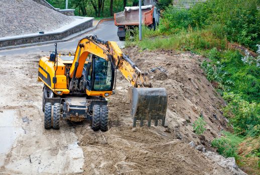 A heavy construction excavator with its bucket levels the sand and backfills the ravine to widen and strengthen the roadway, image with a copy of the space.