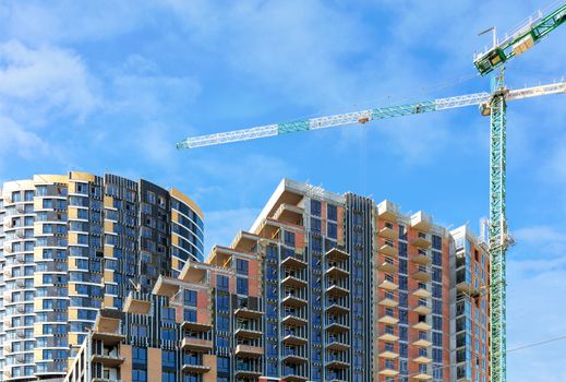 Monolithic-frame cascade concrete structure and tower cranes at the construction site of a multi-storey residential building against a background of blue sky and white clouds, copy space.